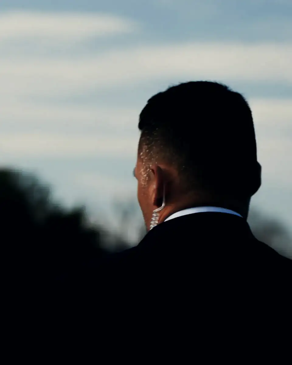 A protection professional in a dark suit, seen from behind at dusk