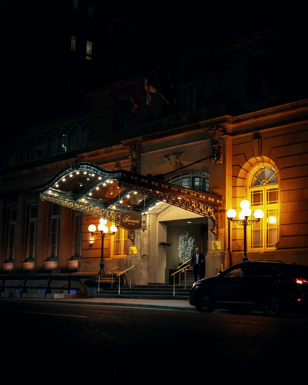 A historic hotel entrance at night with a black car waiting