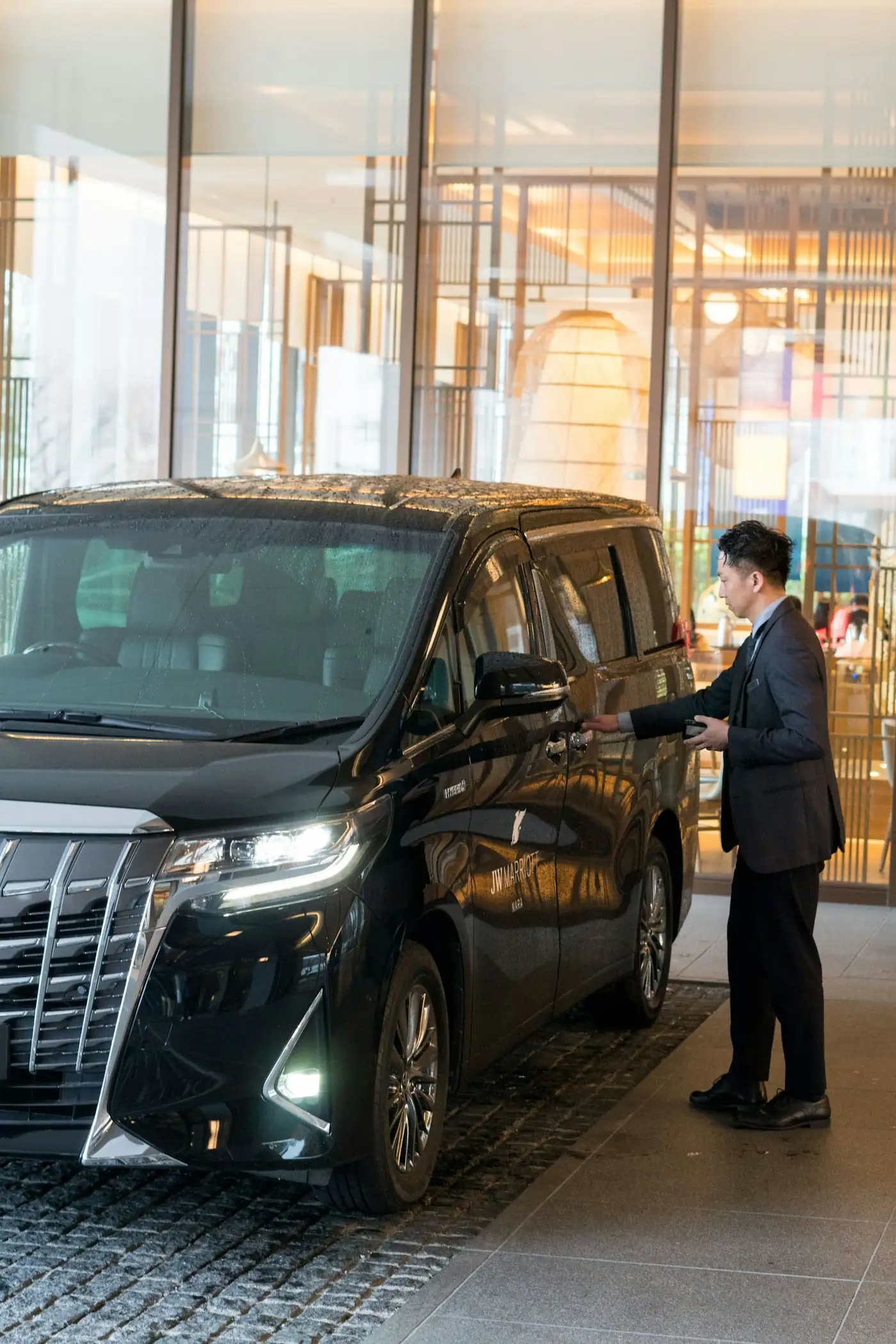 Chauffeur in a suit opening the door of a black van at a hotel entrance