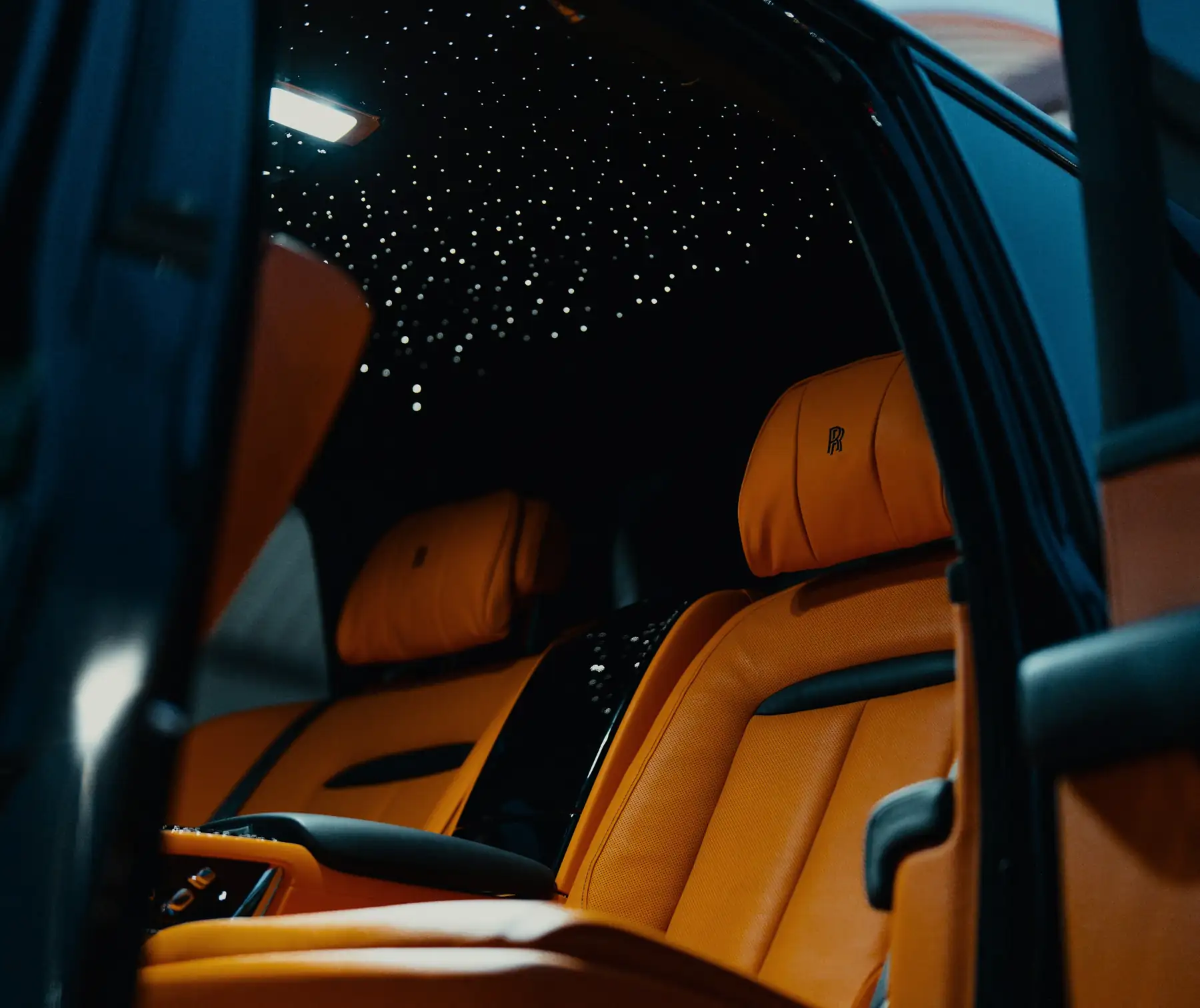 Rear seat of a Rolls-Royce Cullinan under a starlight headliner, seen through the open coach door