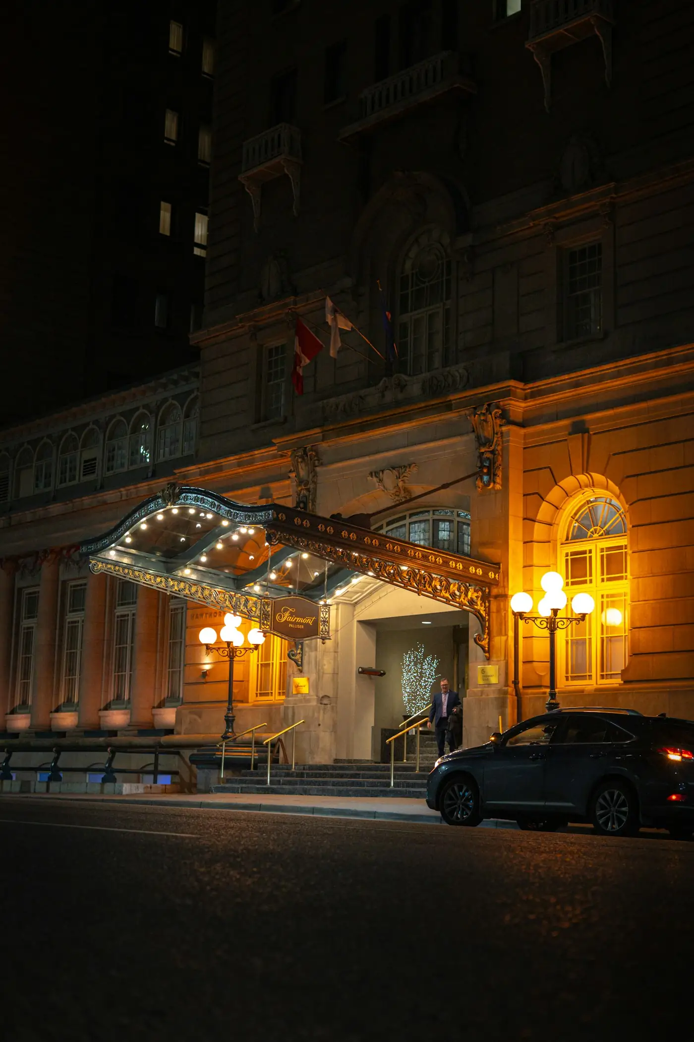 Grand hotel entrance lit warmly at night with a car at the curb