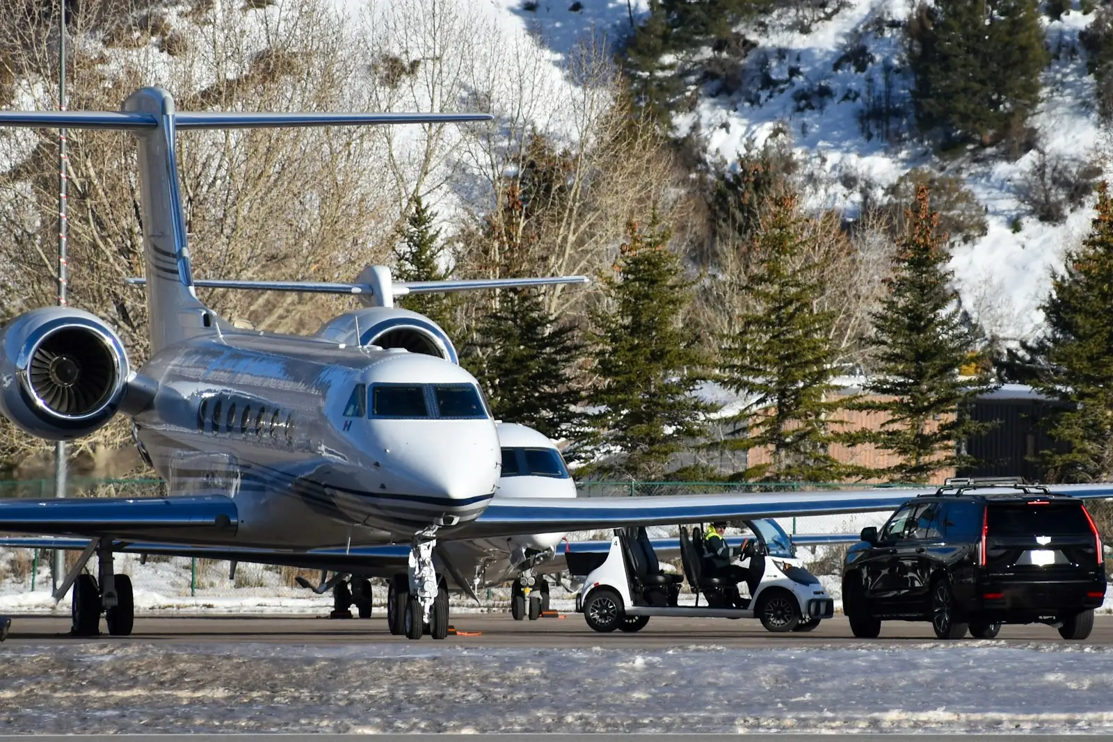 Private jet on a snowy apron with a black SUV parked beside it