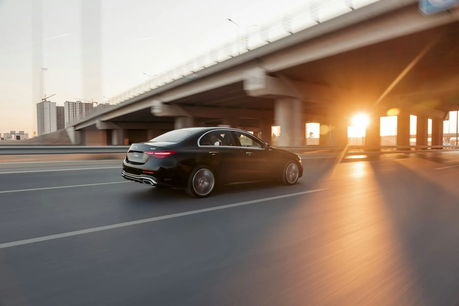 Black Mercedes-Benz sedan driving under a bridge at sunset