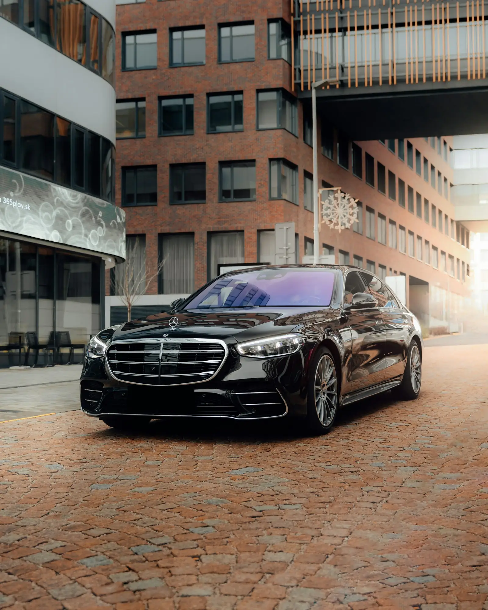Black Mercedes-Benz S-Class on a cobblestone street in front of brick buildings