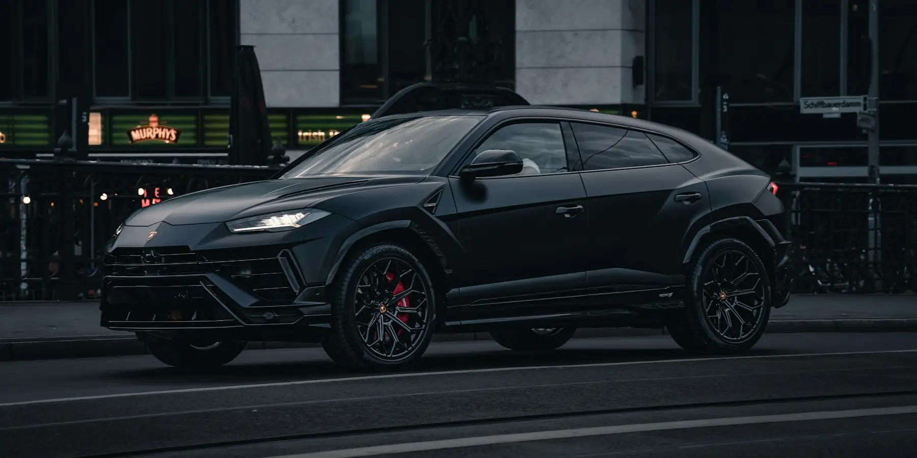 Black Lamborghini Urus parked on a city street at dusk