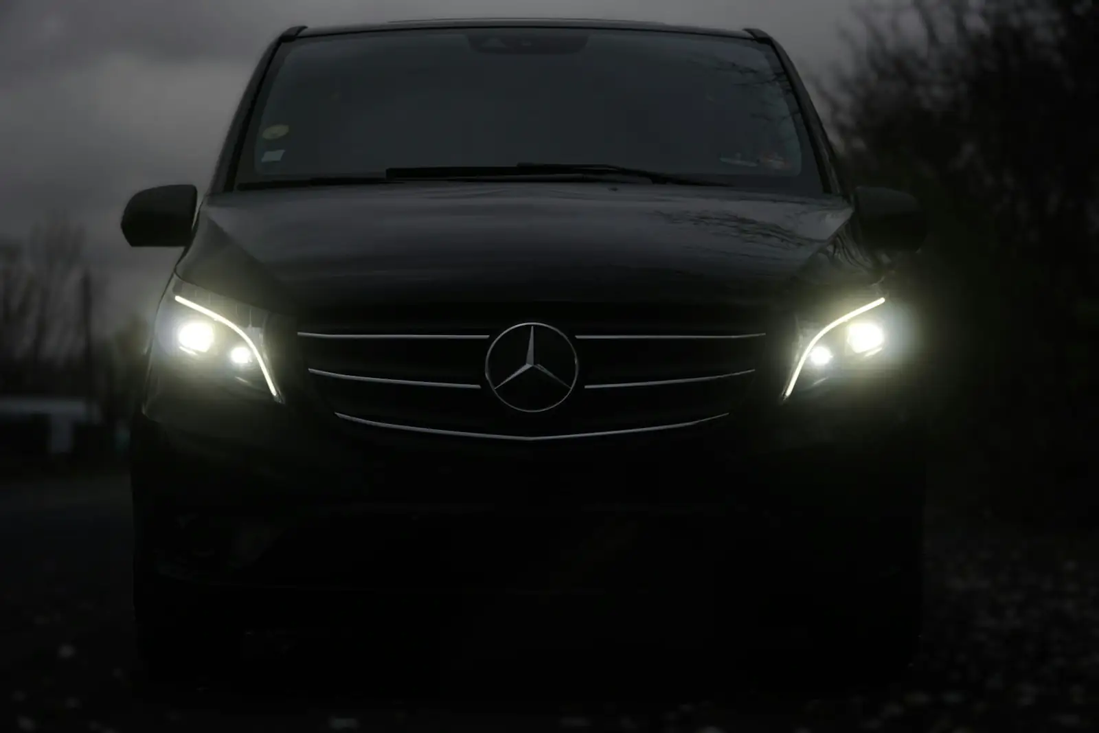 Black Mercedes-Benz van with headlights on in low light