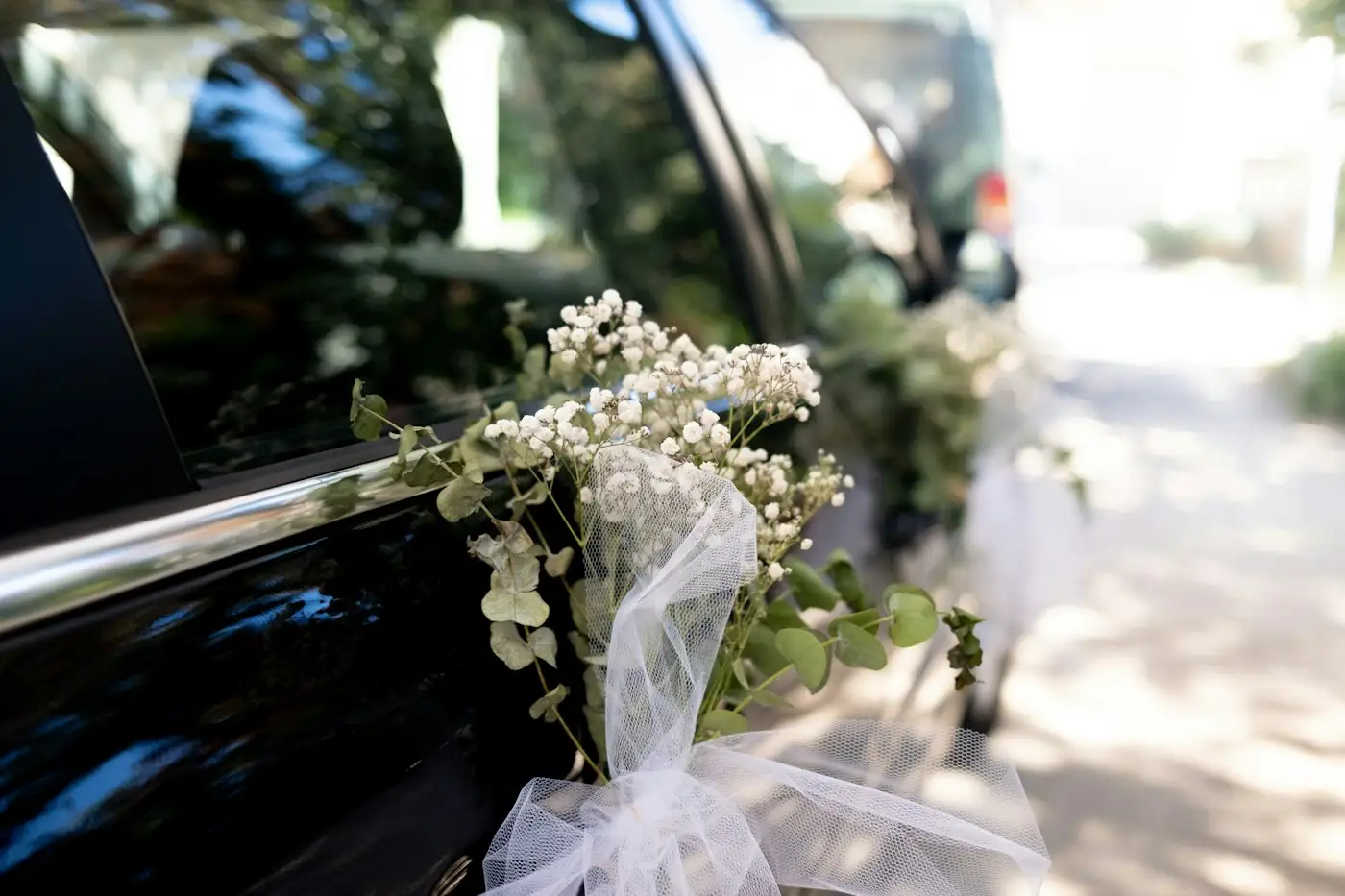 Wedding bouquet with white ribbon tied to the door of a black car